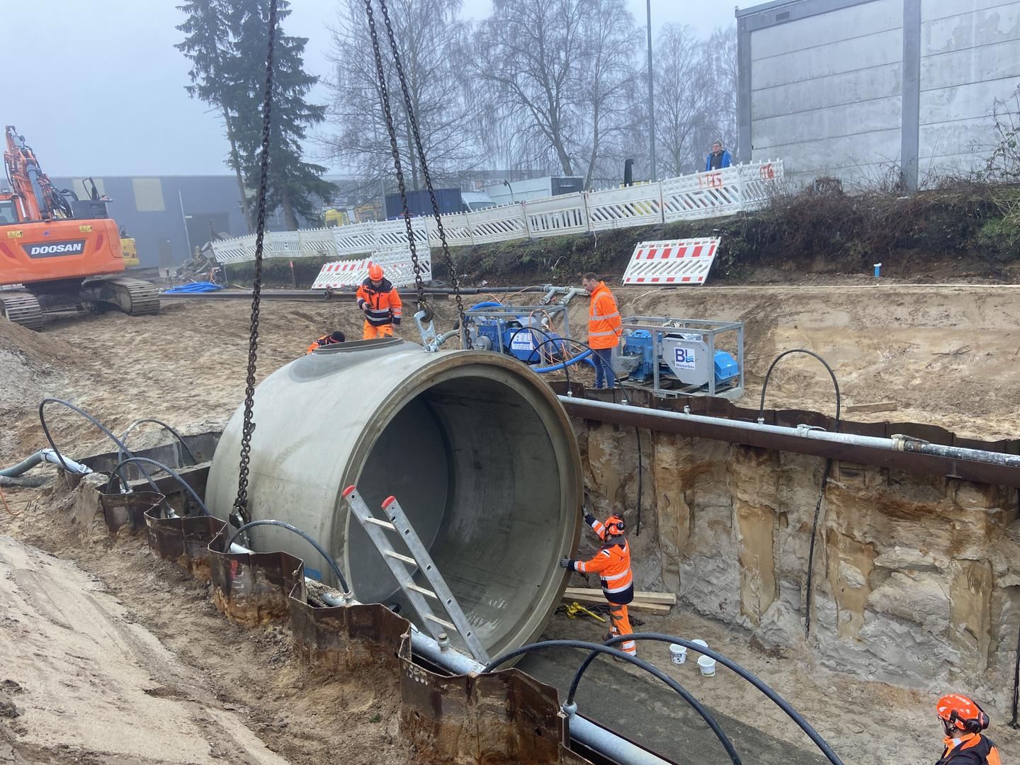 Bauarbeiter platzieren großes Rohr in Bauloch.