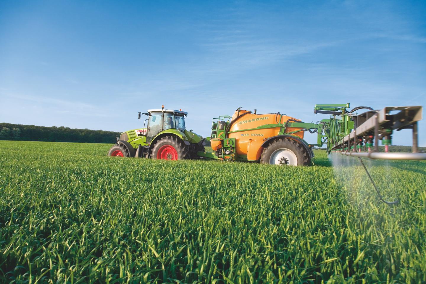 Landwirt bringt mit Traktor Pflanzenschutz auf einem Getreidefeld aus
