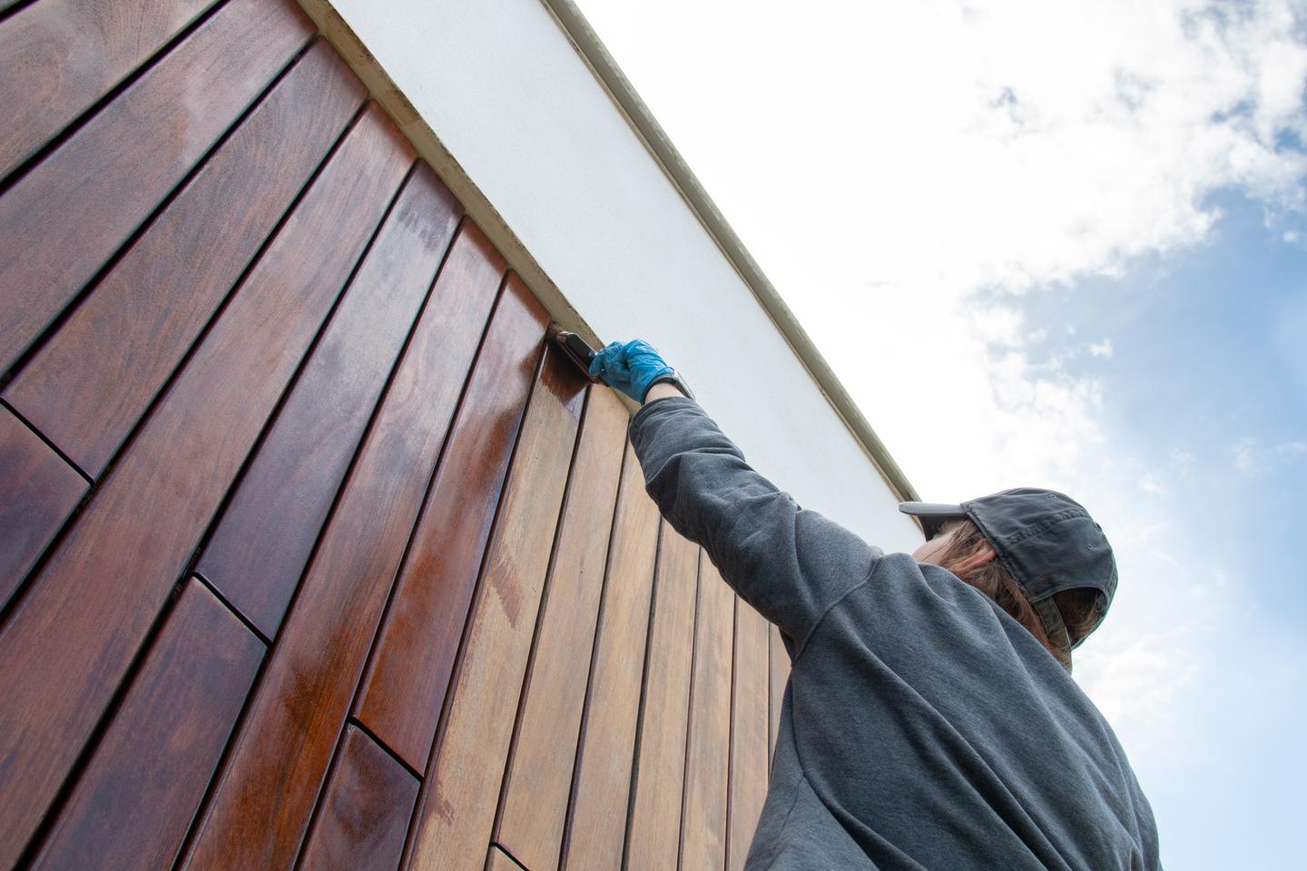 Handwerker ölt Holzpaneele einer Fassade