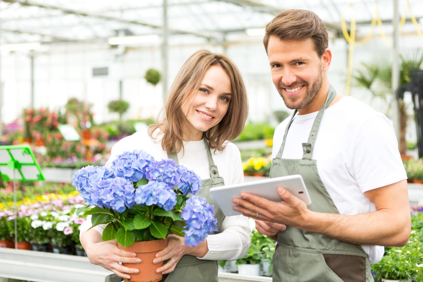 Ein Paar hält in einem Gartenmarkt ein Tablet, um Blumen auszuwählen.