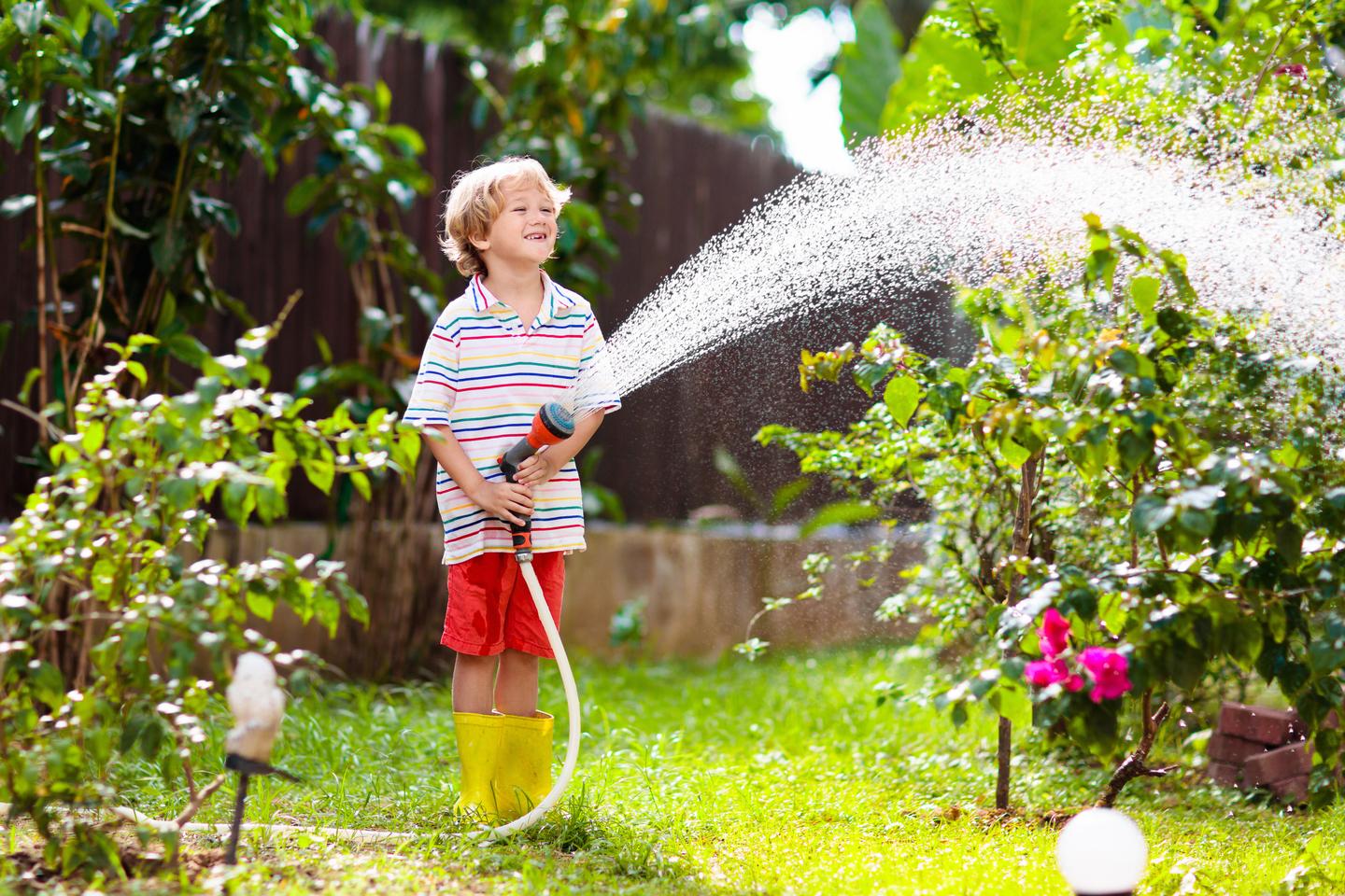 Junge spritzt Wasser mit Gartenschlauch