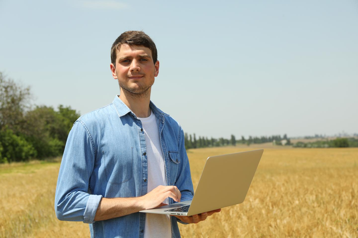 Mann mit Laptop vor Getreidefeld
