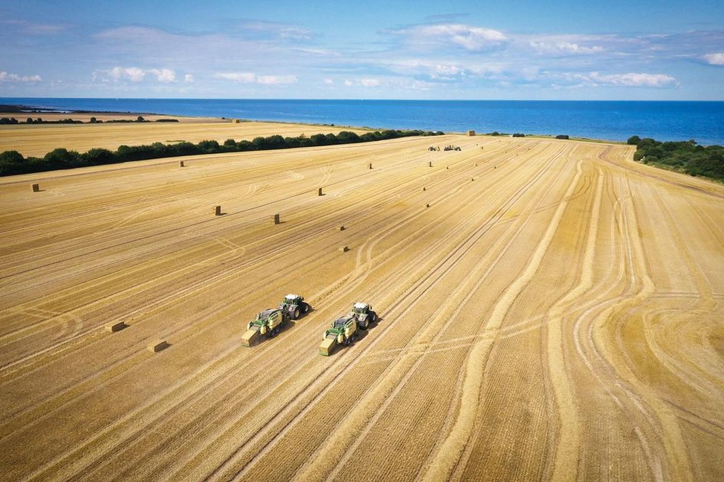 Zwei Traktoren arbeiten auf einem Feld mit dem Meer im Hintergrund.